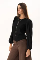 Blusa negra de tejido acanalado con mangas largas abullonadas de textura arrugada y puños elásticos.