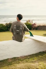 Remeron de algodón color verde musgo con efecto lavado, de manga corta y corte oversize. Presenta una estampa en la espalda con diseño inspirado en la playa, palmeras y flores, junto con la inscripción "Glassy Waves Club".