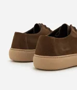 Championes de estilo casual con diseño moc toe, confeccionadas en cuero gamuza color marrón. Presentan costura visible en la puntera, cierre con cordones y suela de goma en tono beige de perfil bajo.