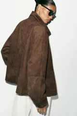 Chaqueta de tejido efecto ante color marrón, con cuello alto, cierre frontal con cremallera y botones a presión, manga larga y bolsillos de plastrón con solapa en el delantero.