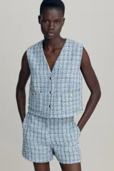 Chaleco sastre en tejido bouclé celeste con detalles en negro y blanco, con escote en V y botones dorados adelante. Modelo ajustado con pinzas en el busto y bolsillos delanteros de parche con botón. Bajo recto con aberturas laterales levemente redondeadas. Forrado.