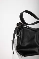 Bandolera Aliada de cuero gris oscuro, con diseño descontracturado, cierre metálico, bolsillo interior y correa ancha regulable con hebilla y argollas metálicas.