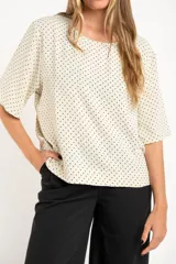Blusa cruda con estampado de lunares negros, de manga corta y cuello redondo.