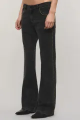 Jeans de denim negro de tiro medio y corte bootcut, con tachas metálicas doradas a lo largo de los laterales y en los bolsillos delanteros.