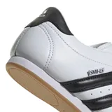 Championes Adidas modelo Taekwondo, color blanco con las icónicas tres tiras laterales en negro. Presentan un diseño minimalista sin cordones, con una lengüeta que cubre el empeine y suela de goma color caramelo.