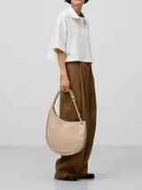 Cartera hobo color beige, de piel sintética con textura craquelada. Tiene un compartimento con cierre de clip magnético y un bolsillo interior con cierre de cremallera. El asa es tubular con pieza metálica y el logo está grabado.