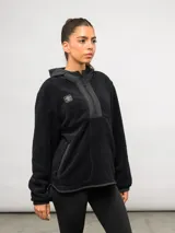 Buzo de polar negro con capucha, cierre frontal parcial y bolsillos laterales. Presenta detalles en nylon a tono en la capucha, la solapa del cierre y los bordes de los bolsillos, con el logo de la marca bordado en el pecho.