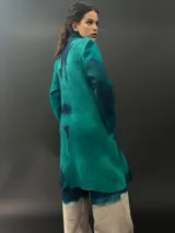 Tapado largo de lana merino color verde con teñido tie-dye en tonos oscuros. Tiene corte particular en los hombros y bolsillos laterales.