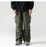 Pantalón cargo de color verde oliva, estilo holgado y técnico, con múltiples bolsillos con solapa y cordones ajustables en cintura y tobillos. Presenta un pequeño logo bordado en blanco en la pierna derecha.