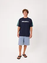 Remera negra de manga corta con diseño deportivo, parte superior de las mangas en color gris con ribete blanco y estampa frontal con la marca Rusty.