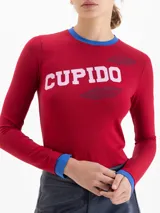Remera de algodón pima con elastano, color rojo, de calce ajustado al cuerpo, manga larga y cuello redondo con detalles en color azul. Presenta estampa frontal con la palabra 'CUPIDO' y diseño de labios.