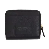 Billetera compacta Marc Jacobs de cuero negro, con cierre perimetral y broche a presión. El interior cuenta con múltiples ranuras para tarjetas y compartimentos para documentos, con herrajes dorados.