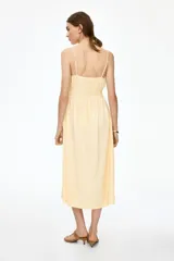 Vestido midi de algodón con textura efecto arrugado, color amarillo, tirantes finos ajustables, escote corazón con abertura tipo cerradura y lazo frontal, cintura elástica fruncida y falda evasé con vuelo ligero.