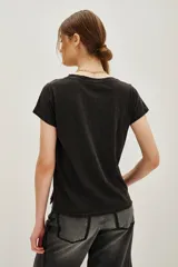 Remera de algodón color negro con efecto lavado, de corte clásico y manga corta. Presenta un estampado frontal con la palabra 'COSMIC' en el centro rodeada por la palabra 'DANCE' repetida en tonos degradados de verde a azul.