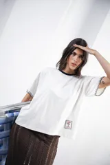 Remera de algodón color azul marino, corte relajado con hombro caído. Presenta cuello redondo blanco y bordado a mano en contraste en los puños de las mangas. Tiene un parche bordado en la parte inferior del frente.