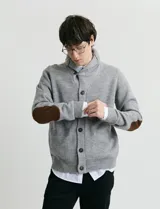 Cardigan de punto color marrón con cuello esmoquin, cierre frontal con botones y presilla superior. Presenta mangas largas con coderas en contraste y bolsillos frontales de ribete.