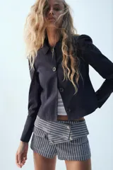 Blazer corta de color azul marino, con cuello solapa y cierre frontal con botones. Cuenta con manga larga con frunces en los hombros.