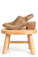Zueco destalonado de cuero color camel, con diseño perforado en el empeine, tira ajustable con hebilla en el talón y taco cuadrado bajo de madera.