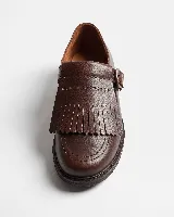 Mocasín de cuero natural color marrón, con costuras visibles, hebilla lateral metálica y solapa desmontable con flecos.