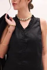 Top negro sin mangas con frente de lino, escote en V y volados decorativos alrededor del cuello y la abertura frontal.