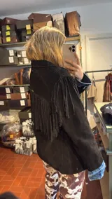 Campera de gamuza color marrón con diseño de flecos largos en la parte superior delantera, espalda y mangas. Presenta solapas clásicas, corte recto y cierre frontal con botones.