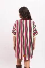 Vestido camisola de tejido de punto fresco con rayas verticales en tonos fucsia, verde oscuro, beige y rosado. Presenta cuello polo marrón, mangas cortas y cierre frontal con botones de madera.