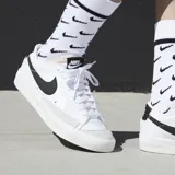 Championes Nike Blazer Low 77 de corte bajo, con capellada de cuero blanco, logo Swoosh lateral en negro y refuerzo de gamuza en la puntera. Presenta suela de goma con textura y lengüeta con espuma expuesta.