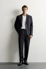 Pantalón de traje relaxed fit color negro, confeccionado en tejido con lana, con bolsillos frontales, bolsillos traseros de doble vivo con botón y raya marcada en las piernas.