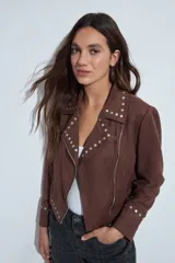 Campera estilo biker de símil gamuza color marrón, con cierre frontal y detalles de tachas metálicas en solapas, mangas y ruedo.