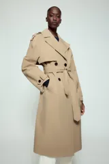 Trench largo de color negro con cuello de solapa, manga larga con trabillas ajustables y cierre frontal cruzado con doble botonadura. Cuenta con bolsillos delanteros de vivo, solapa cortavientos en el pecho y cinturón ajustable del mismo tejido.