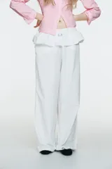 Pantalón blanco de nylon, tiro alto, con cintura elástica y detalle de sobrefalda o peplum superpuesto con hebilla metálica. Corte ancho y pierna recta.