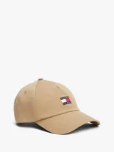 Gorra de béisbol de algodón en color beige, con diseño clásico de cinco paneles, ojales de ventilación y visera curva. Presenta un parche bordado con el logo de Tommy Jeans en la parte frontal y cuenta con una hebilla metálica ajustable en la parte trasera.
