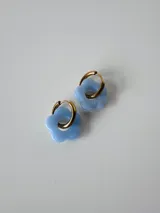 Aros de acero quirúrgico dorados tipo argolla con dije colgante en forma de flor color celeste.
