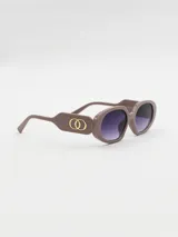 Lentes de sol con armazón de acetato color visón, diseño ovalado y patillas anchas con detalle de eslabones dorados entrelazados. Lentes con degradado oscuro.