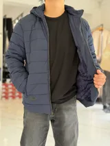Campera puffer azul marino con capucha ajustable, cierre frontal y bolsillos laterales con cierre a presión. Cuenta con parche redondo con la inscripción "TURK" en el pecho.