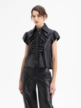 Camisa de cuero ovino negra, con volados en el centro delantero, mangas con volumen fruncidas en la copa y broches forrados en cuero.