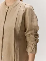 Camisa de lino liviano color tostado, con silueta relajada, cuello mao, alforzas verticales frontales, mangas con volumen y puños elastizados con volados.
