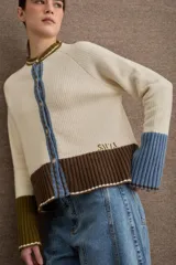 Cardigan de punto con diseño color block en tonos bordó, verde oliva y beige. Presenta cuello redondo con detalle en celeste, cierre frontal con botones y puños acampanados en color beige.