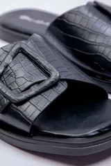 Sandalias planas Paddock modelo Amelias, de color negro con textura efecto cocodrilo. Presentan una tira ancha en el empeine decorada con una hebilla grande cuadrada del mismo material y tono.