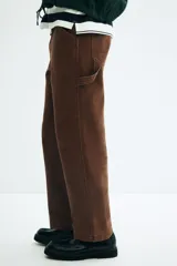 Pantalón worker marrón de sarga de algodón gruesa, con piernas rectas y corte relaxed fit. Presenta cintura clásica con cierre de botón, bolsillos al bies, bolsillo monedero, bolsillos traseros, trabilla funcional en un lateral y bolsillo cargo dividido en dos en el otro.