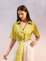 Camisa corta de color verde lima, con textura arrugada, cuello camisero, escote en V y nudo frontal. Mangas cortas y holgadas.