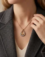 Collar de acero con baño de oro, compuesto por una cadena fina y un dije colgante en forma de lágrima con diseño bicolor en tonos dorado y plateado.