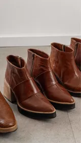 Botinetas de cuero color marrón con diseño de punta fina, plataforma negra y taco cuadrado de madera. Presentan una banda de cuero sobre el empeine y cierre lateral.