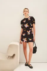 Vestido corto de cuello redondo con estampado floral multicolor sobre fondo negro. Presenta mangas cortas con detalle fruncido en los hombros y aberturas laterales en la cintura.