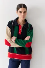 Buzo de punto con cuello polo y cierre frontal de tres botones. Presenta un diseño a rayas verticales en tonos beige y marrón, con mangas en bloques de color rojo y detalles en rosa en los puños y el ruedo.