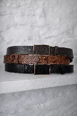 Cinturón de cuero con textura de reptil, disponible en tres colores (negro, marrón y tostado). Incluye hebillas intercambiables de diseño ovalado y rectangular con acabado metálico.