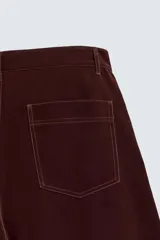 Pantalón de hombre color bordó oscuro, de corte ancho (wide fit), confeccionado en tejido de algodón con acabado flocada o efecto aterciopelado. Presenta cinco bolsillos y cierre frontal con cremallera y botón.