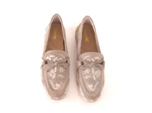 Mocasín de gamuza color avena con bordados florales en hilo blanco y pequeños apliques metálicos dorados. Presenta un lazo decorativo en la capellada y suela de goma flexible.