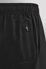 Pantalones cortos deportivos color marrón rojizo, confeccionados en tejido técnico ligero y elástico. Presentan cintura elástica ajustable con cordón interior, bolsillos frontales y un bolsillo trasero con cierre de cremallera. Los laterales tienen perforaciones para transpirabilidad y aberturas laterales en el bajo.