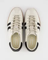 Championes deportivos de estilo retro color blanco con detalles en negro, suela fina color caramelo, capellada de cuero y nylon, lengüeta semitransparente acolchada, cordones bicolor intercambiables y cuello acolchado.